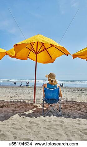 Picture - Rear view of female tourist sitting under beach umbrella, Camana, Arequipa, Peru. Fotosearch