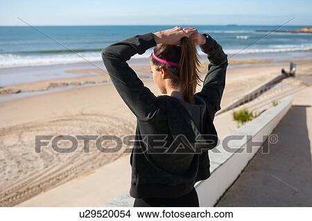 Picture - Rear view of young woman at beach tying hair in ponytail, Carcavelos, Lisboa, Portugal, Europe. Fotosearch