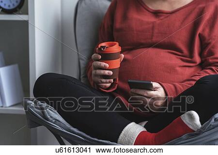 Stock Image - Relaxed pregnant woman using smartphone.. Fotosearch