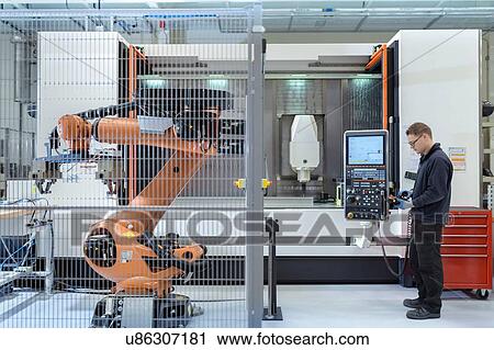 Stock Image - Robotics engineer operating robot aided CNC machine in robotics research facility. Fotosearch