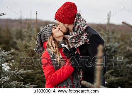 Picture - Romantic young couple kissing while shopping for christmas tree from forest. Fotosearch