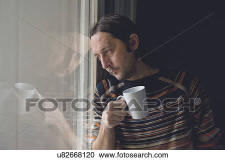 Stock Image - Sad man by window drinking coffee.. Fotosearch
