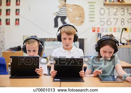 Stock Image - Schoolboy and girls listening to headphones in class at primary school. Fotosearch