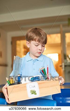 Stock Photograph - Schoolboy carrying box of pencils in classroom at primary school. Fotosearch