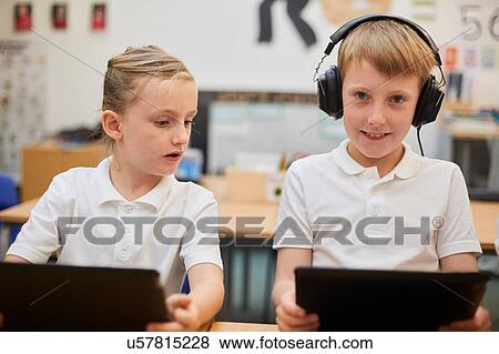 Stock Photo - Schoolboy listening to headphones in class at primary school, portrait. Fotosearch