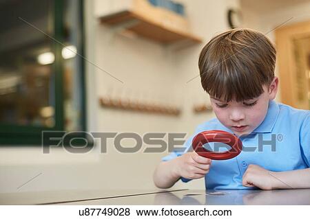 Stock Photo - Schoolboy looking through magnifying glass in classroom lesson at primary school. Fotosearch