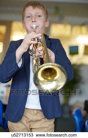Stock Image - Schoolboy playing trumpet in primary school classroom. Fotosearch