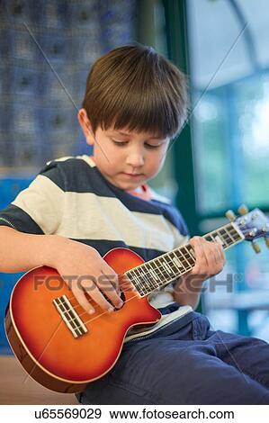 Stock Photo - Schoolboy playing ukulele in classroom at primary school. Fotosearch