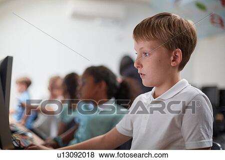 Stock Photo - Schoolboy using computer in classroom at primary school. Fotosearch