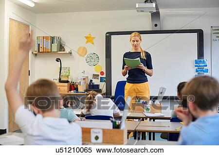 Stock Photography - Schoolboy with hand raised in classroom lesson at primary school. Fotosearch