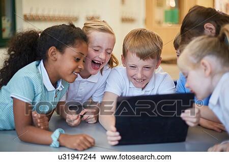 Picture - Schoolboys and girls laughing at digital tablet in classroom at primary school. Fotosearch