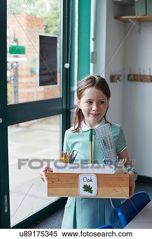 Stock Photography - Schoolgirl carrying box of pencils in classroom at primary school. Fotosearch