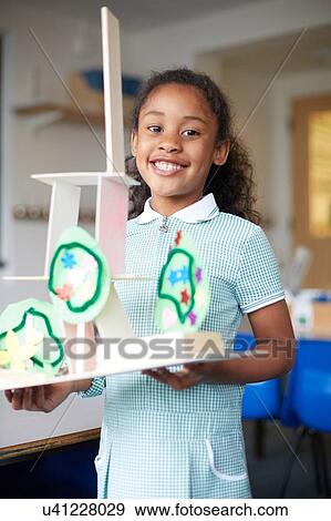 Stock Photo - Schoolgirl holding cardboard model in classroom at primary school, portrait. Fotosearch