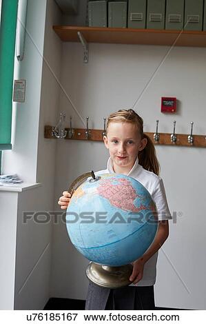 Stock Photo - Schoolgirl holding globe in classroom at primary school, portrait. Fotosearch