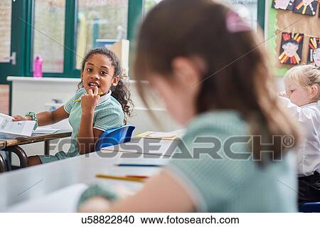 Stock Image - Schoolgirl looking over her shoulder in classroom at primary school. Fotosearch