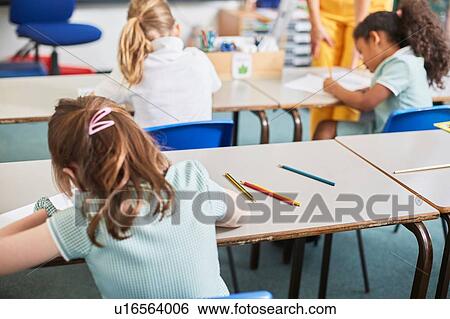 Stock Photograph - Schoolgirl writing at classroom desk in primary school lesson, rear view. Fotosearch