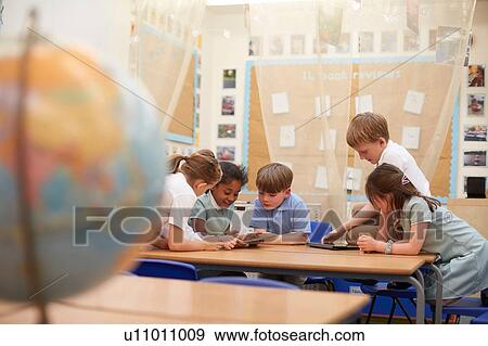 Stock Photo - Schoolgirls and boys looking at digital tablets in classroom lesson at primary school. Fotosearch