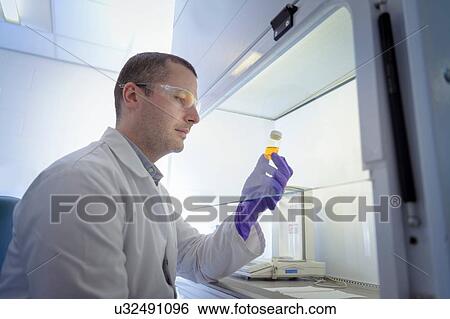 Stock Photograph - Scientist inspecting pharmaceutical sample in fume cupboard in laboratory. Fotosearch