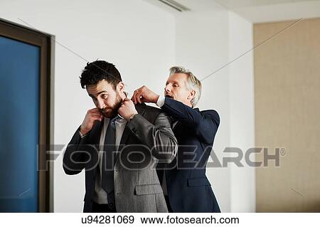 Stock Photo - Senior businessman adjusting colleague's jacket in office. Fotosearch
