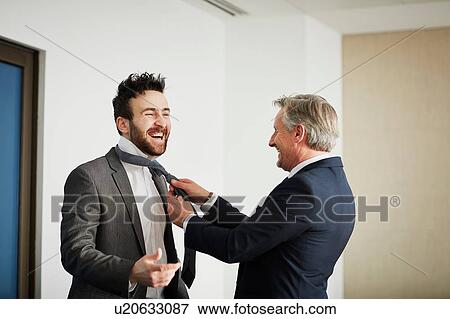 Stock Photo - Senior businessman fastening colleague's tie in office. Fotosearch