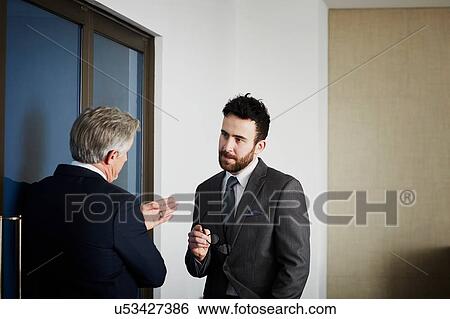 Stock Photograph - Senior businessman having discussion with male colleague in office. Fotosearch