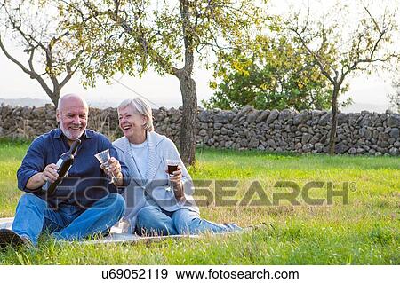 Stock Photo - Senior couple outdoors, sitting on blanket, enjoying glass of wine. Fotosearch