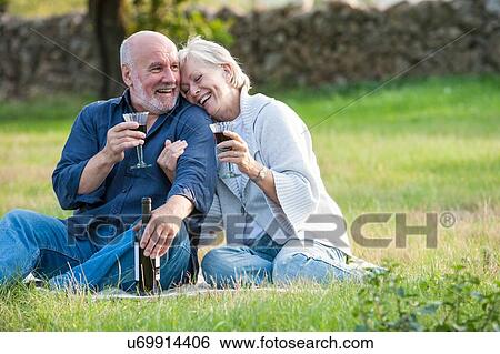 Stock Photograph - Senior couple outdoors, sitting on blanket, enjoying glass of wine. Fotosearch