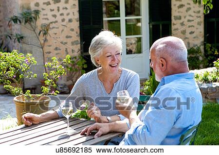 Stock Photography - Senior couple sitting in garden, enjoying glass of wine. Fotosearch