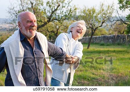 Senior couple walking in rural setting, holding hands, fooling around View Large Photo Image Stock Photo - Senior couple walking in rural setting, holding hands, fooling around. Fotosearch