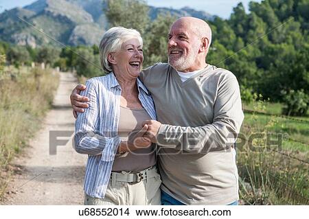 Senior couple walking together in rural setting, holding hands, smiling View Large Photo Image Picture - Senior couple walking together in rural setting, holding hands, smiling. Fotosearch