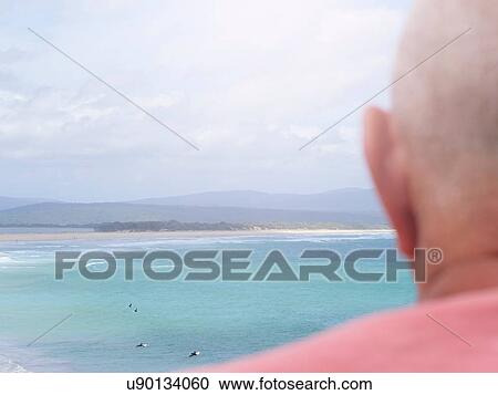Stock Image - Senior man looking at coastal view, rear view, Mallacoota, Victoria, Australia. Fotosearch