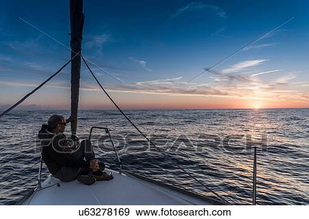 Stock Photo - Senior man sitting aboard yacht watching sunset, Porquerolles, Provence-Alpes-Cote d'Azur. Fotosearch