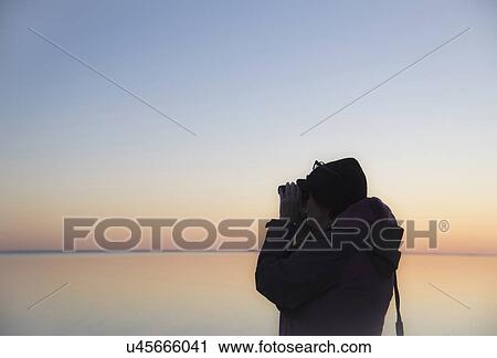 Stock Image - Senior woman birdwatching at sunset. Fotosearch