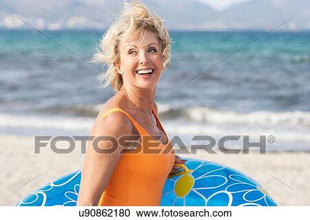 Stock Image - Senior woman carrying inflatable on beach, Palma de Mallorca, Spain. Fotosearch
