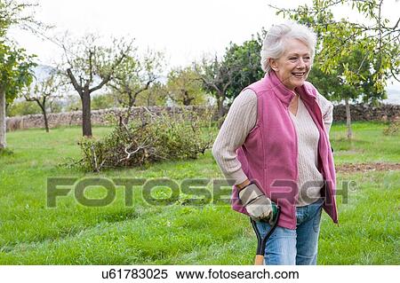 Stock Photography - Senior woman in garden, leaning on gardening tool. Fotosearch