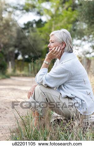 Stock Photography - Senior woman sitting in rural setting, thoughtful expression. Fotosearch