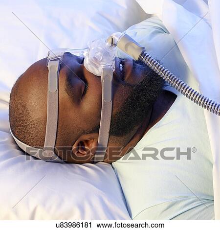 Stock Image - Sleeping man wearing ventilator to treat sleep apnoea.. Fotosearch