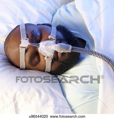 Stock Image - Sleeping man wearing ventilator to treat sleep apnoea.. Fotosearch