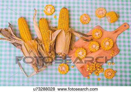 Stock Photo - Sliced corn on the cob on chopping board, with whole corn on cob, overhead view. Fotosearch