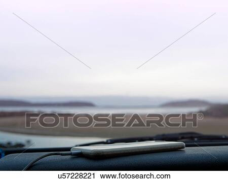 Stock Image - Smartphone on car dashboard, coastal view seen through car windscreen, Broulee, New South Wales, Australia. Fotosearch