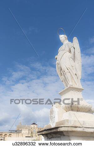 Stock Image - Spain, Andalusia, Cordoba, Statue of San Rafael against clouds. Fotosearch