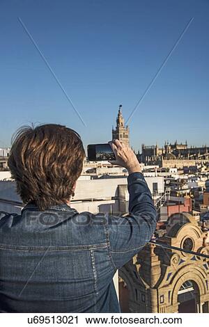 Spain, Andalusia, Seville, Plaza Nueva, Woman taking photo of cityscape and la Giralda with smartphone View Large Photo Image Stock Image - Spain, Andalusia, Seville, Plaza Nueva, Woman taking photo of cityscape and la Giralda with smartphone. Fotosearch