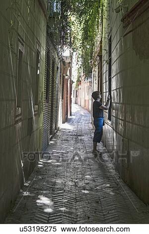 Stock Photography - Spain, Seville, Woman taking photo with cell phone in backstreets of Judeira. Fotosearch