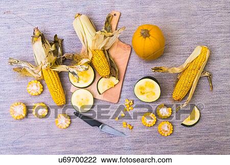 Stock Image - Still life of corn on the cob with two varieties of squash, whole and sliced, overhead view. Fotosearch