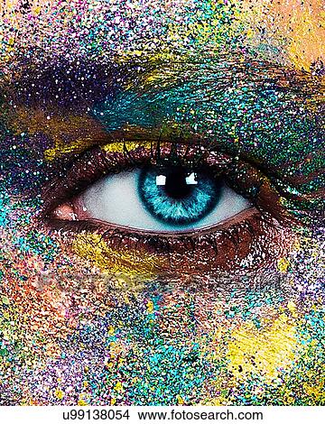 Picture - Studio portrait of blue eyed young woman with glittery multi coloured powder on face, close up of eye. Fotosearch