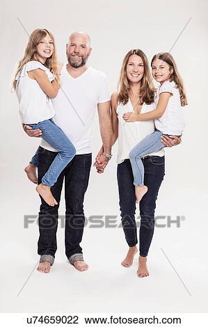Stock Image - Studio portrait of mature couple carrying two daughters, full length. Fotosearch