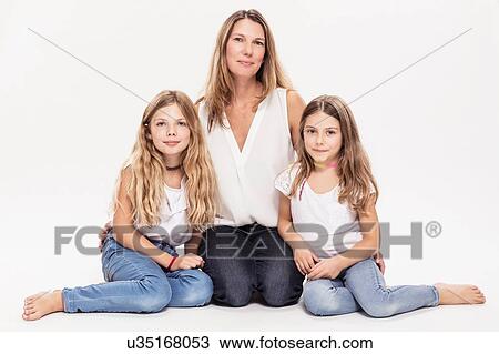 Stock Image - Studio portrait of mature woman with two daughters sitting on floor. Fotosearch