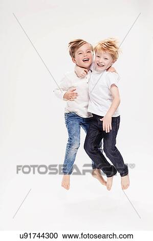 Stock Image - Studio portrait of two boys jumping mid air, full length. Fotosearch