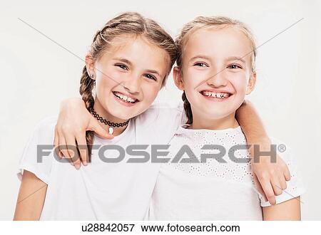 Stock Photo - Studio portrait of two girls with arms around each other, head and shoulders. Fotosearch