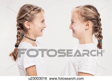 Stock Photograph - Studio portrait of two girls with hair plaits face to face, head and shoulders. Fotosearch